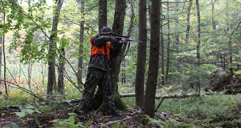 Camouflaged hunter aiming down a rifle in the woods